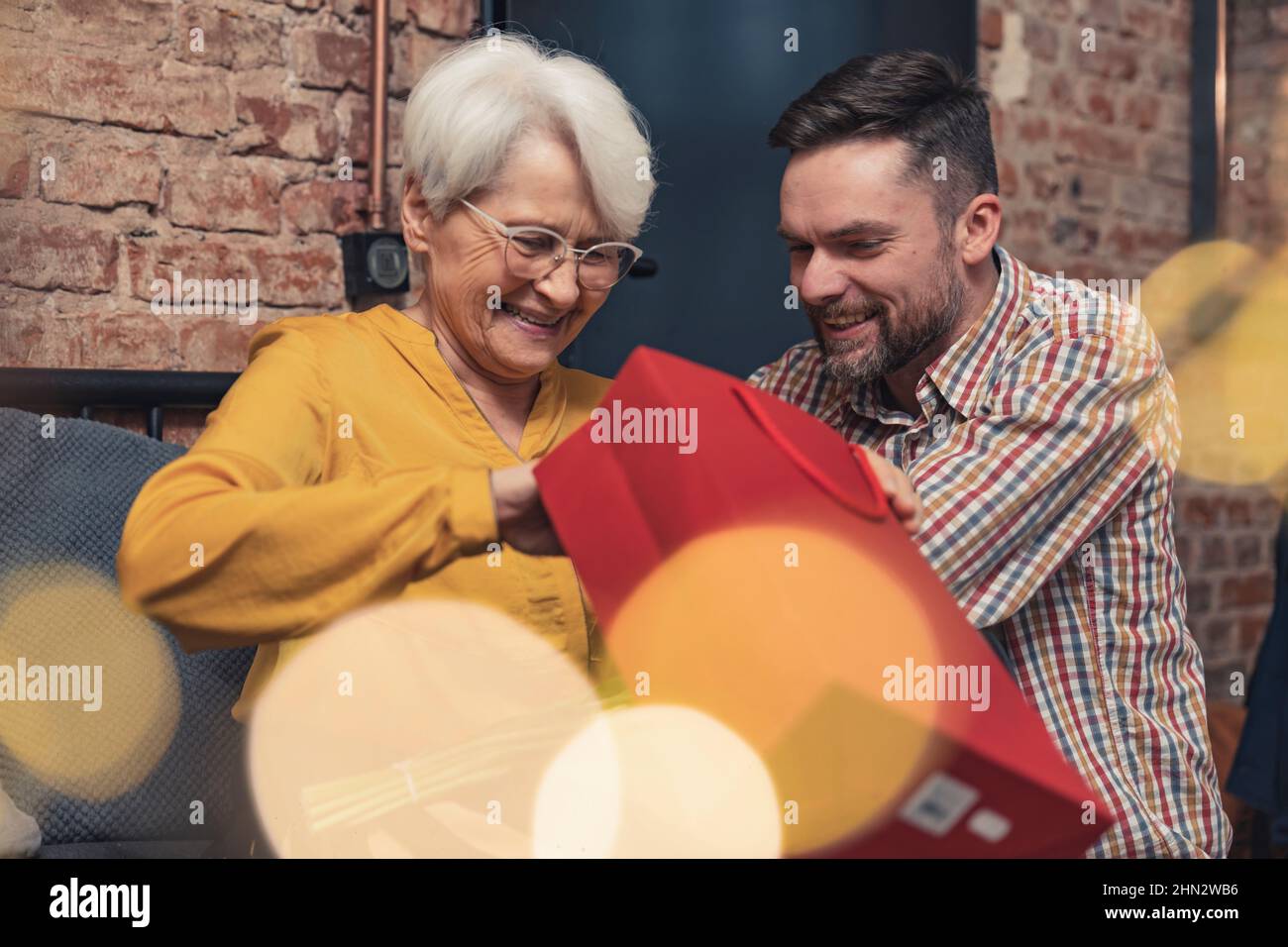 Schöne Mutter mittleren Alters sitzt mit erwachsenem Sohn hält Geschenk und lachend Muttertag Oma's Day Licht Blinkschuss. Hochwertige Fotos Stockfoto