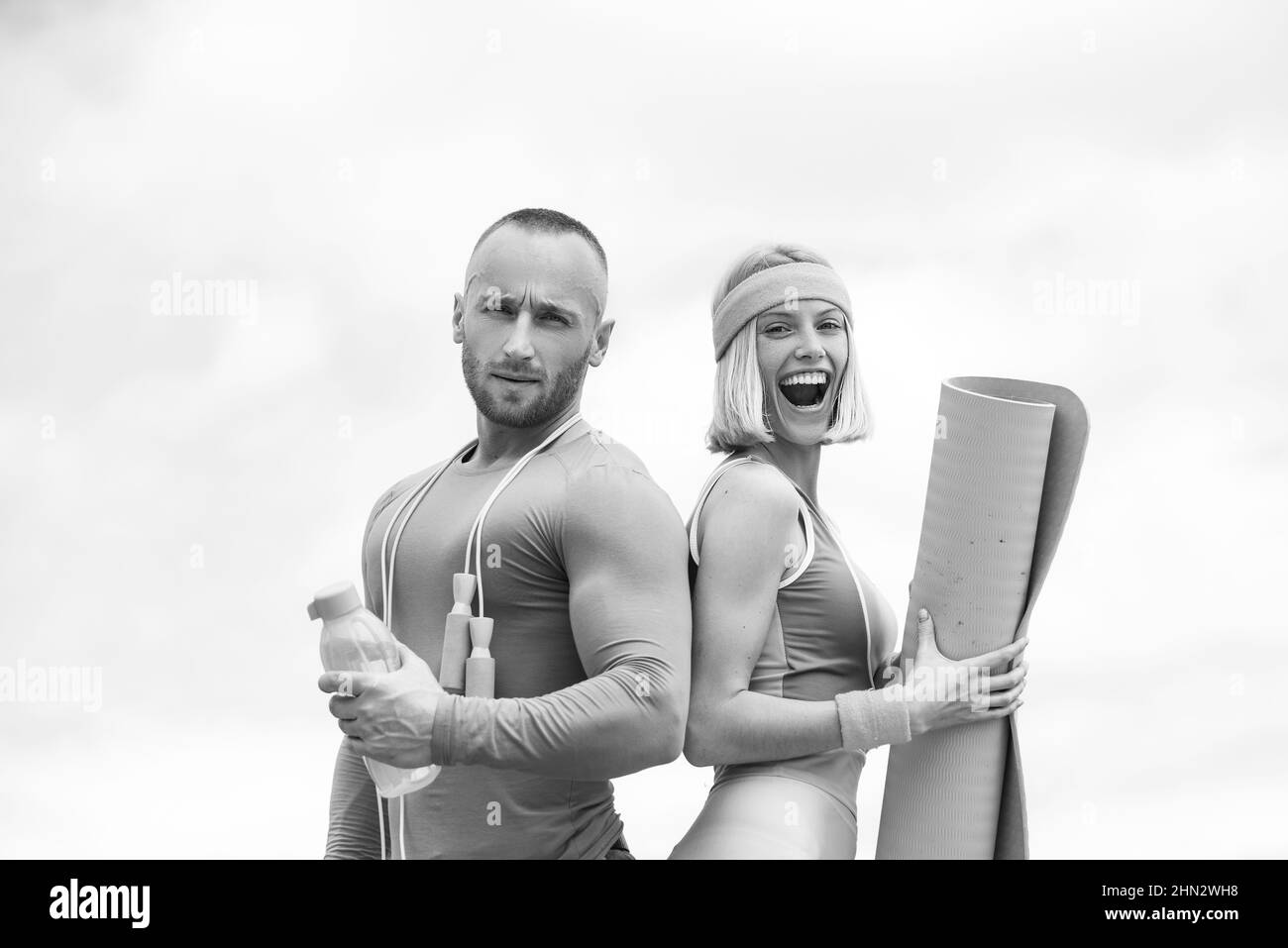 Junge schöne Paar macht Sport-Übungen. Starker, gutaussehender Mann, der eine Flasche Wasser mit einer Yogamatte neben einer jungen Sportlerin hält. Trends Stockfoto