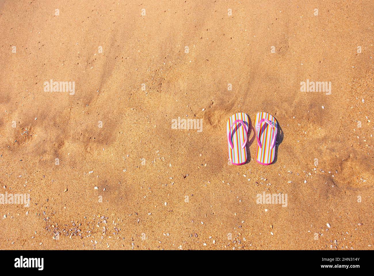 Ein Paar rosa Kinderflipflops auf glattem Sand bietet auf der linken Seite Platz zum Kopieren für jede Urlaubs- und Urlaubseinnahme. Stockfoto