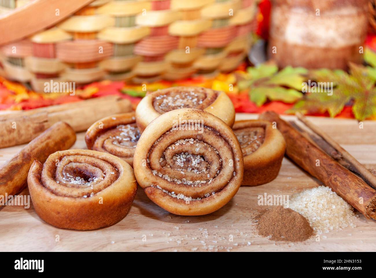 Festliche Herbststimmung mit frisch gebackenen Zimtschnecken, umgeben von Zimtrinde und Herbstfarben. Stockfoto