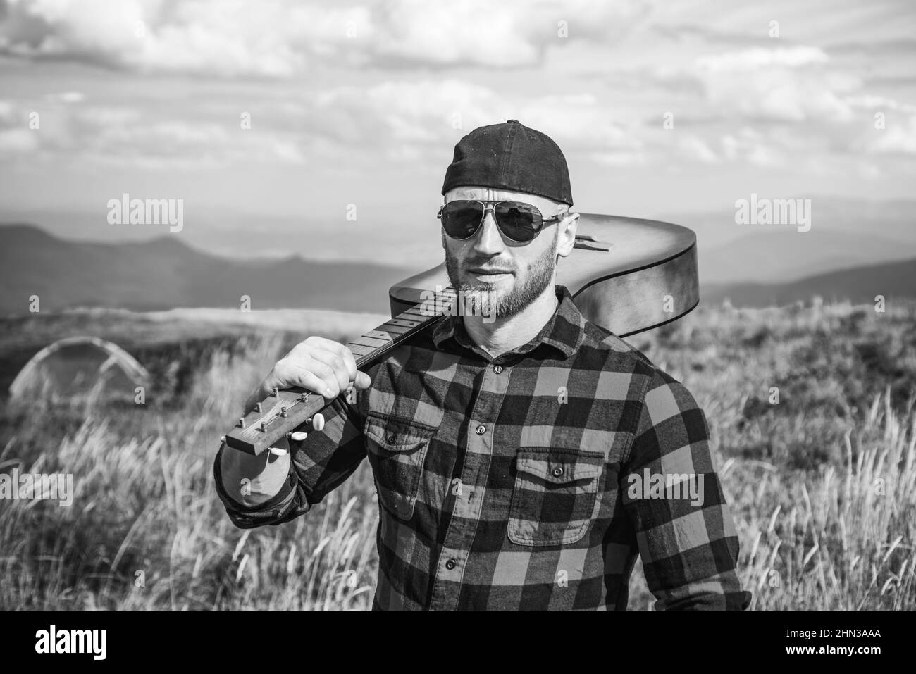 Wanderer Mann mit Gitarre Blick auf schöne Aussicht. Camping-Urlaub. Mann Hipster Wanderer in den Bergen. Porträt des selbstbewussten Menschen. Stockfoto