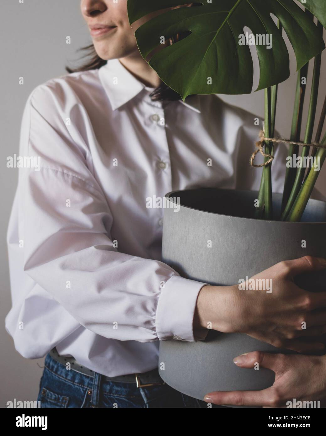Die junge Frau steht mit einem großen Blumentopf mit Monstera Stockfoto