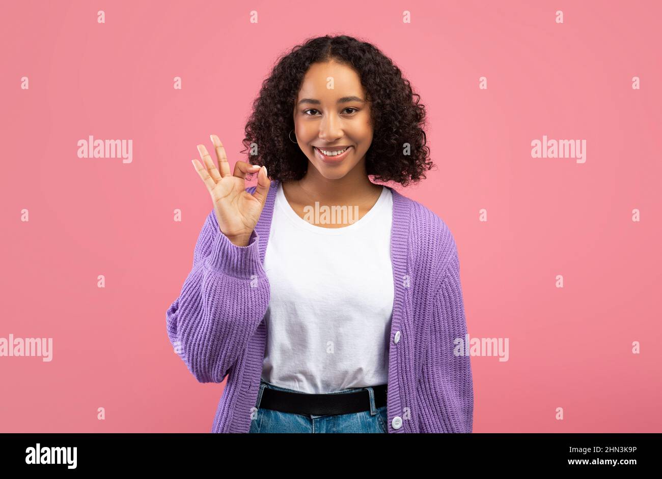Lächelnde junge afroamerikanische Frau, die eine gute Geste zeigt, etwas auf rosa Hintergrund billigt oder empfiehlt Stockfoto