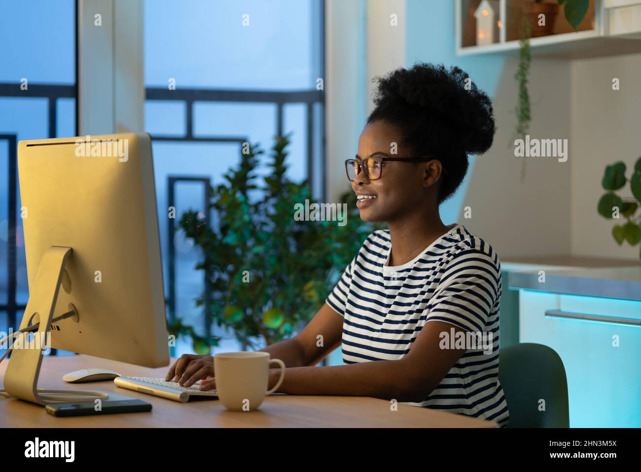 Junge glückliche afrikanische Frau Fernarbeiterin trägt eine Brille, die am Computer tippt, und genießt freiberuflichen Job Stockfoto