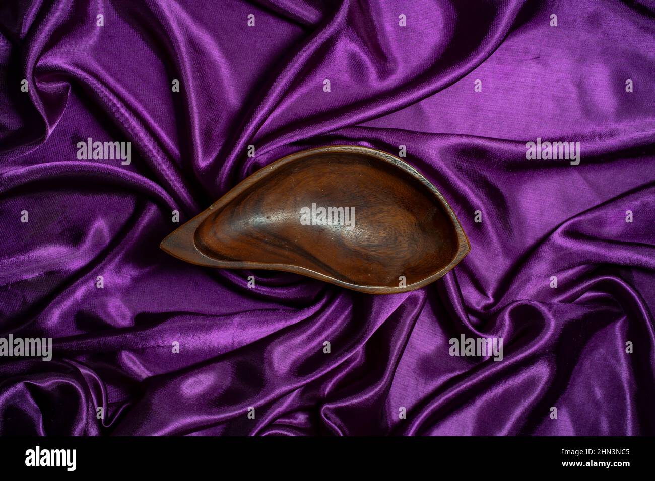 Tropfenhohe Holzschale auf violettem Satin-Wellen-Hintergrund Stockfoto