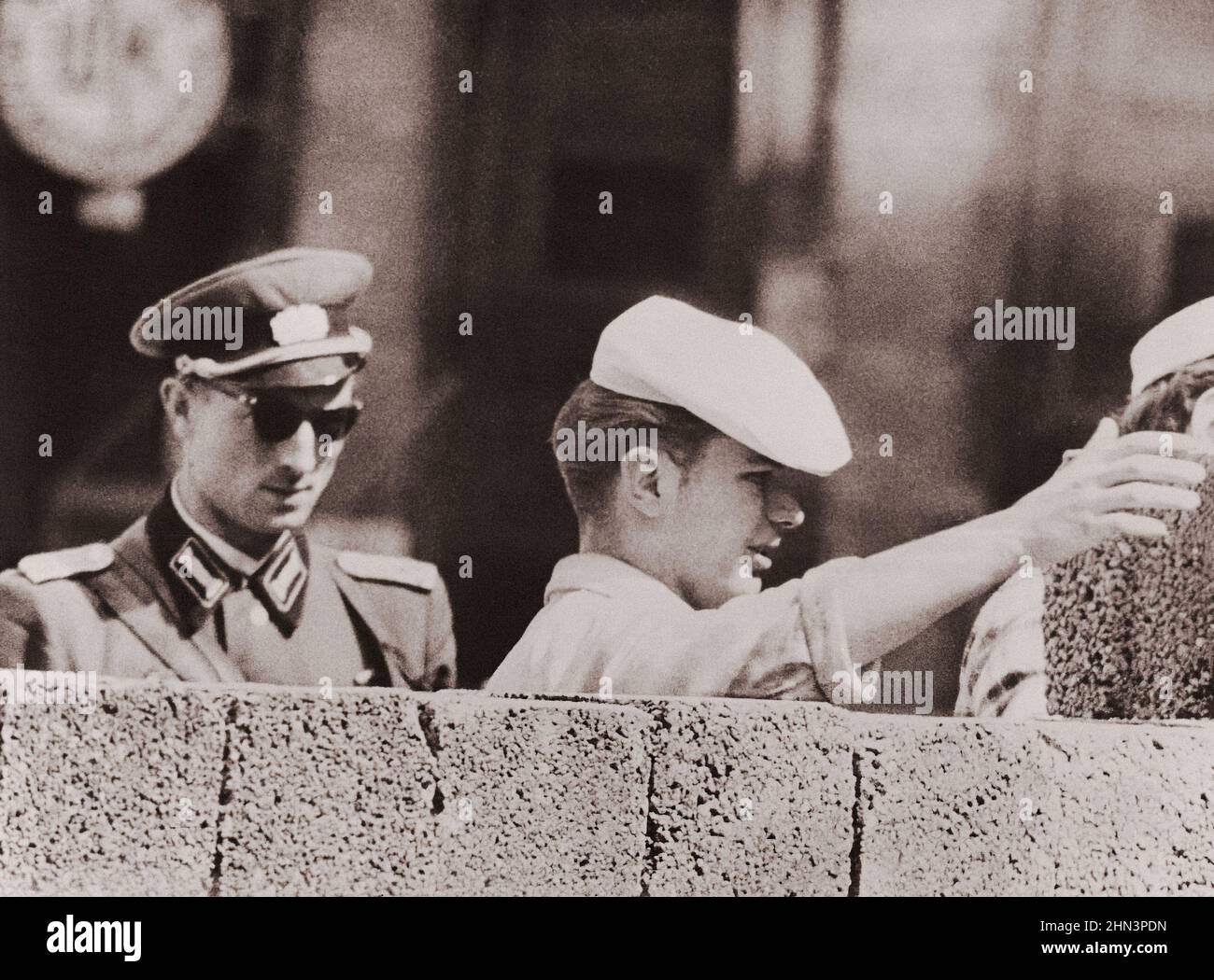 Vintage-Foto der Berliner Krise von 1961: Mauerbau. Ein Ost-Berliner Freimaurer, der von Einem kommunistischen Polizisten sorgfältig beobachtet wird, verdoppelt die Höhe der Stockfoto