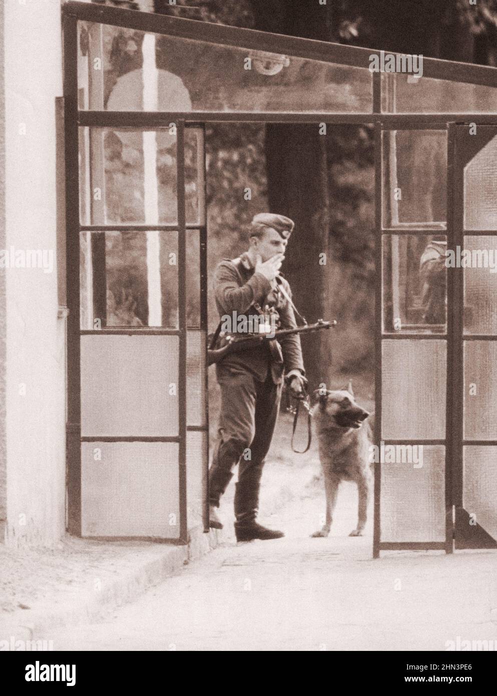 Vintage-Foto der Berliner Krise von 1961: Mauerbau. Mit Wachhund und Maschinenpistole beobachtet dieses Mitglied der Volkspolizei aktiv Stockfoto