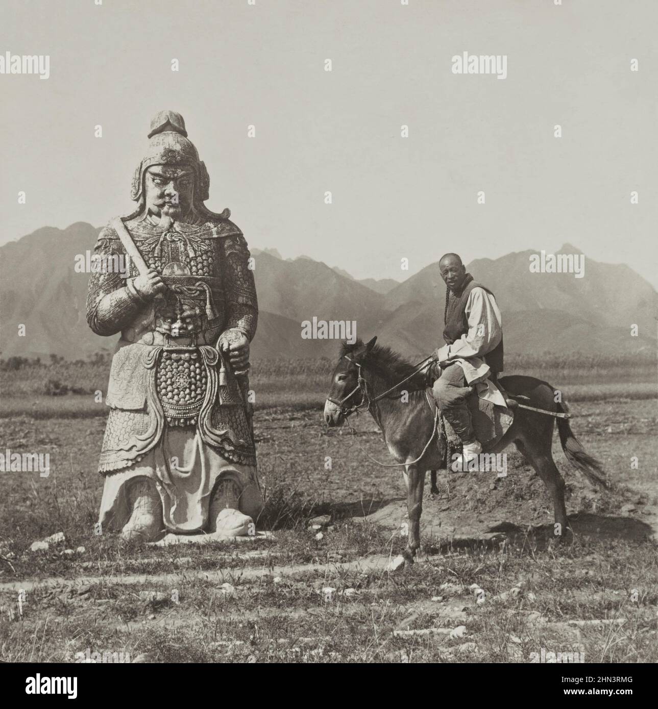 Vintage-Foto des chinesischen Mannes in traditioneller Kleidung und mit Schlange auf einem Esel in der Nähe eines Steinsoldaten in der berühmten Allee der Steintiere (Ming Stockfoto