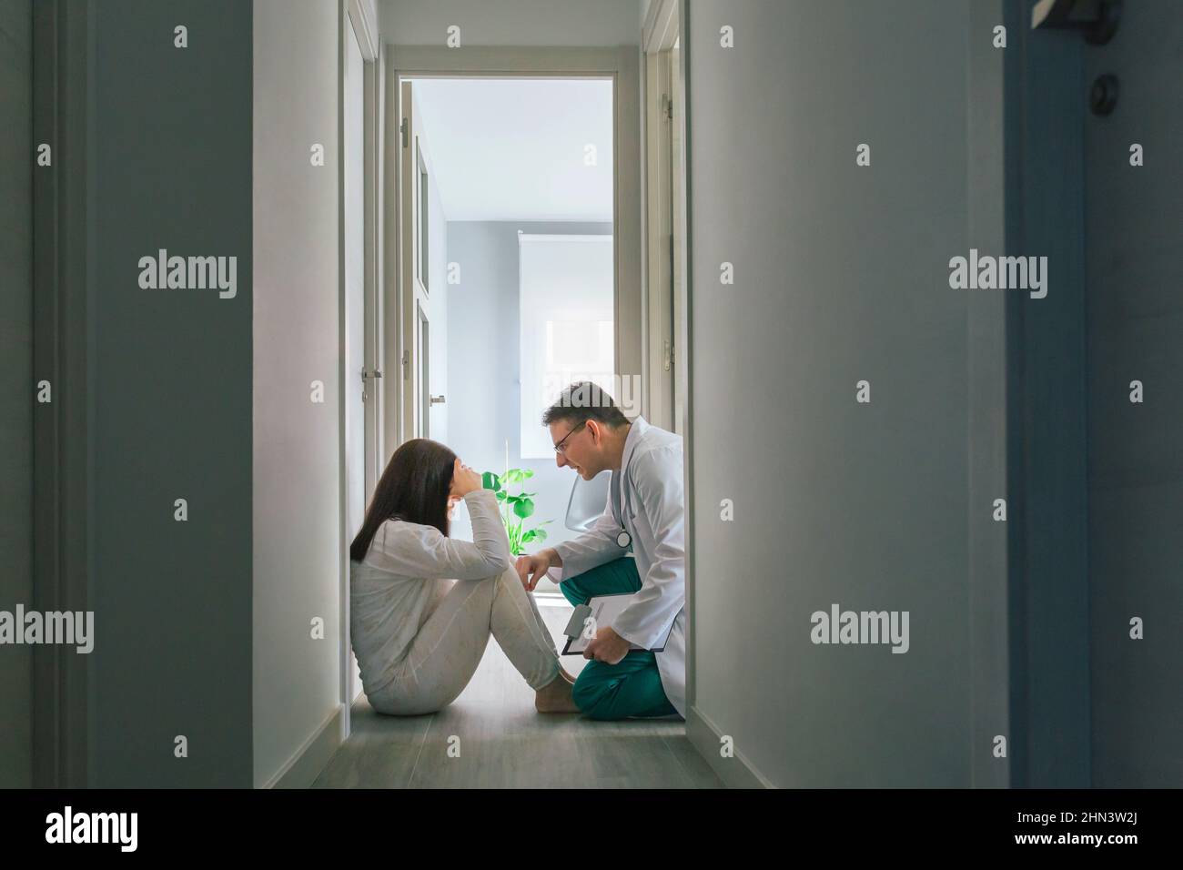 Arzt beruhigt mit Empathie eine Patientin, die auf dem Boden eines psychiatrischen Zentrums sitzt Stockfoto