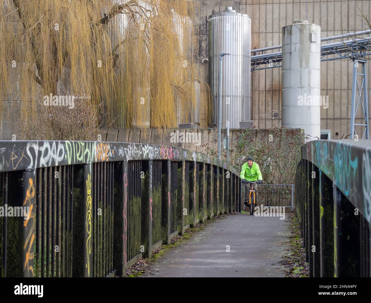 Ein Graffiti sprühte eine Fußgängerbrücke vor einem industriellen Hintergrund, Northampton, Großbritannien; ein Radfahrer überquerte die Brücke Stockfoto