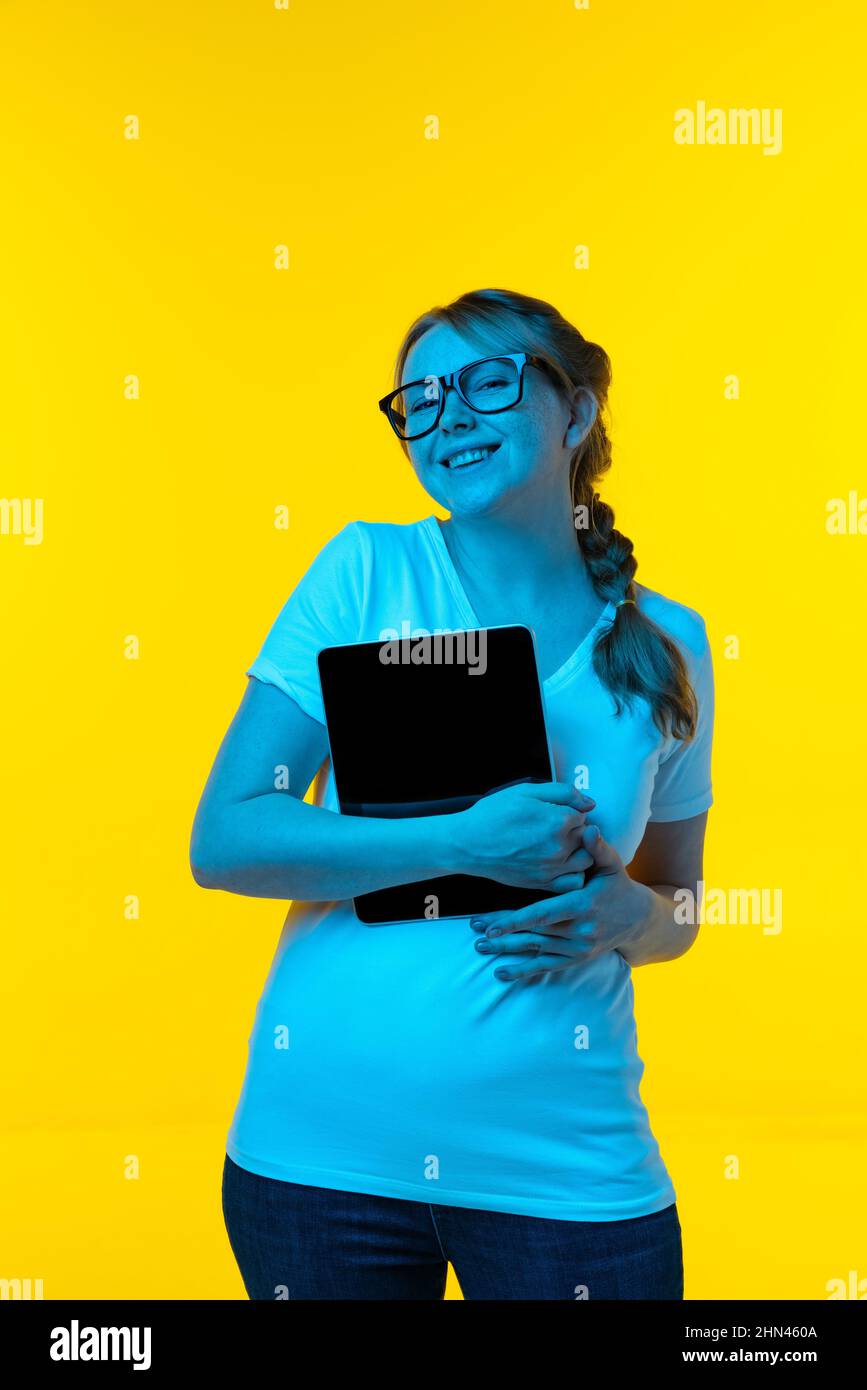 Schönes junges Mädchen mit Sommersprossen auf ihrem Gesicht isoliert auf gelbem Hintergrund in Neon. Konzept der Wow Emotionen, Mimik, Werbung, Verkauf Stockfoto