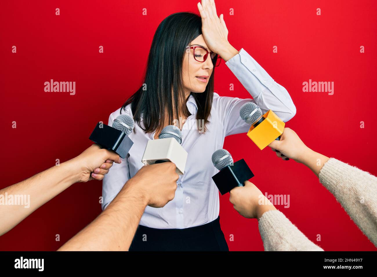 Junge hispanische Frau, die für Journalisten Hände mit Mikrofon mit Hand auf Kopf für Fehler überrascht interviewt, erinnern Fehler. vergessen, schlechtes Memor Stockfoto