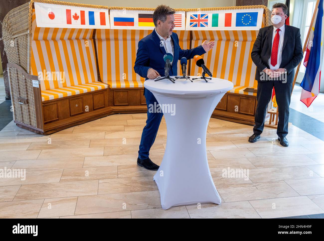 14. Februar 2022, Mecklenburg-Vorpommern, Schwerin: Bundesminister für Wirtschaft und Klimaschutz, Robert Habeck (Bündnis 90/die Grünen), beantwortet neben Reinhard Meyer (SPD, r), Minister für Wirtschaft, Tourismus und Verkehr Mecklenburg-Vorpommerns, Während einer Pressekonferenz im Wirtschaftsministerium Mecklenburg-Vorpommerns vor einem Strandstuhl mit den Flaggen verschiedener Länder. Habeck besucht nach einem Treffen mit dem Landesabteilungsleiter Meyer die insolventen MV Shipyards Group und das Wasserstoffenergieunternehmen Apex in Rostock-Laage. Stockfoto