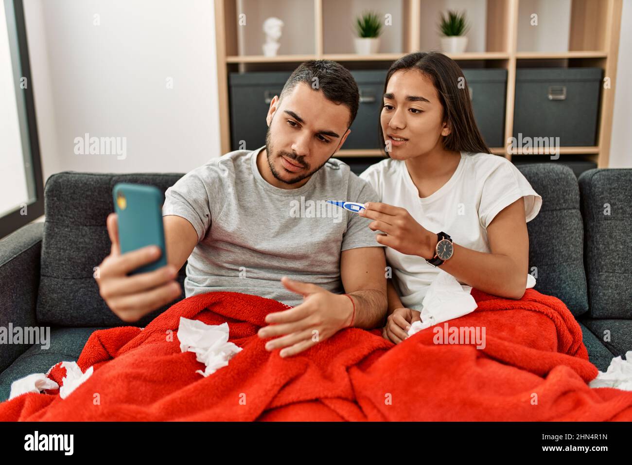 Junges lateinamerikanisches krankes Paar, das zu Hause eine medizinische Fernsultation mit dem Smartphone hat. Stockfoto