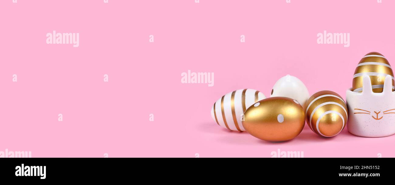 Rosa Osterbanner mit Eiern mit Punkten und Streifen, niedlicher Eierbecher in Form von Hase auf rosa Hintergrund Stockfoto