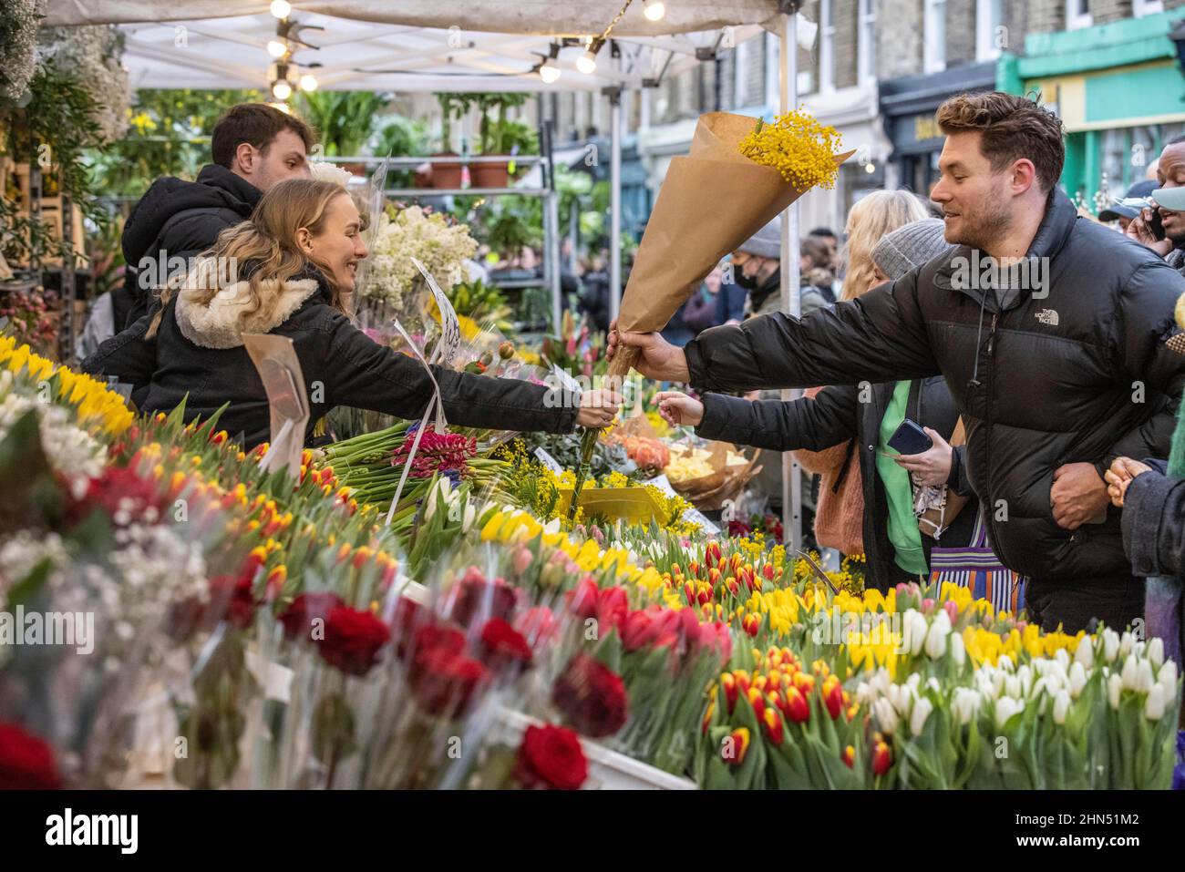 Columbia Road Flower Market beschäftigt mit Ausstellern, die ihre Blumenstände arrangieren und Menschen, die vor dem Valentinstag, East London, Großbritannien, Blumen kaufen Stockfoto