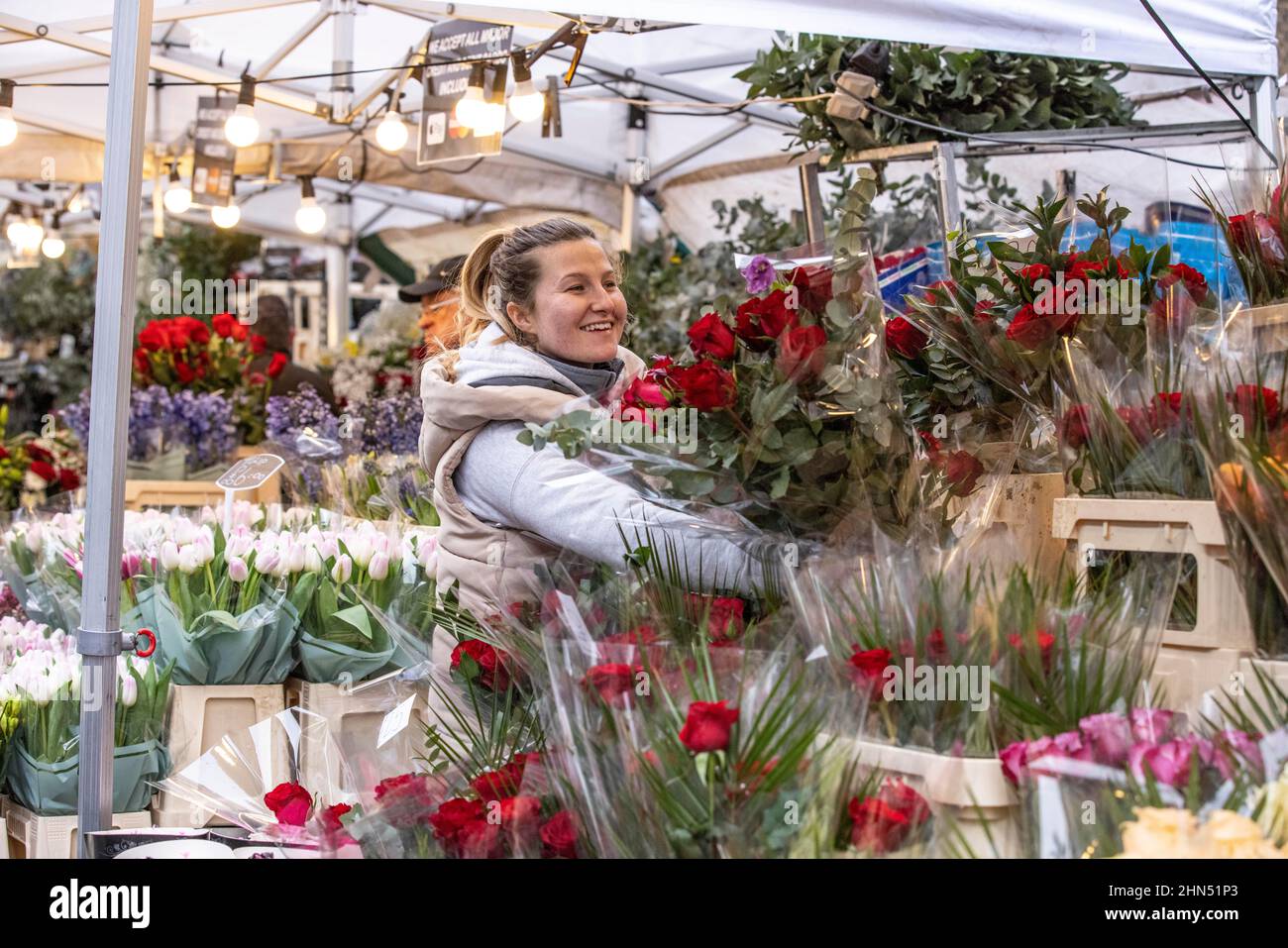Columbia Road Flower Market beschäftigt mit Ausstellern, die ihre Blumenstände arrangieren und Menschen, die vor dem Valentinstag, East London, Großbritannien, Blumen kaufen Stockfoto