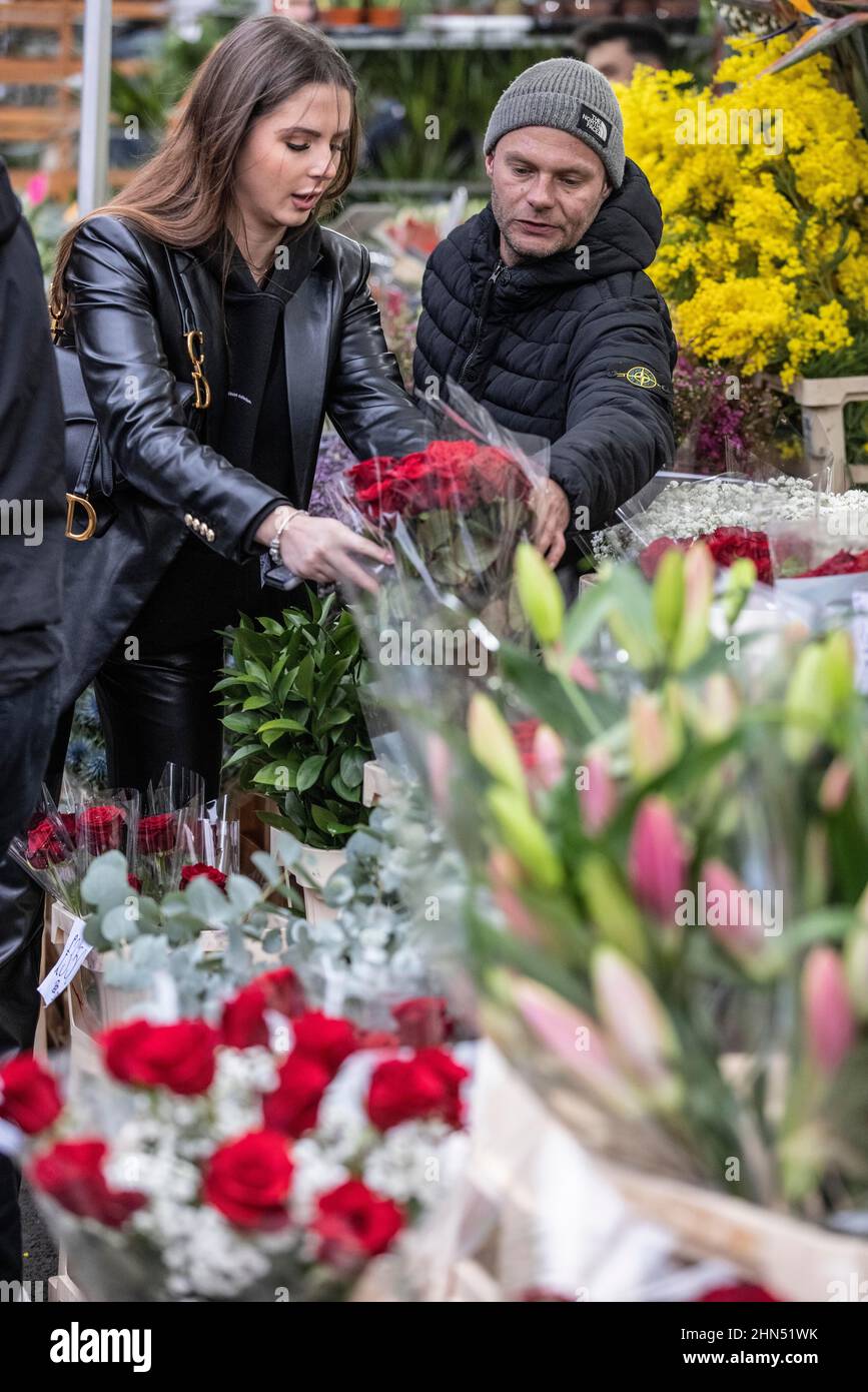 Columbia Road Flower Market beschäftigt mit Ausstellern, die ihre Blumenstände arrangieren und Menschen, die vor dem Valentinstag, East London, Großbritannien, Blumen kaufen Stockfoto