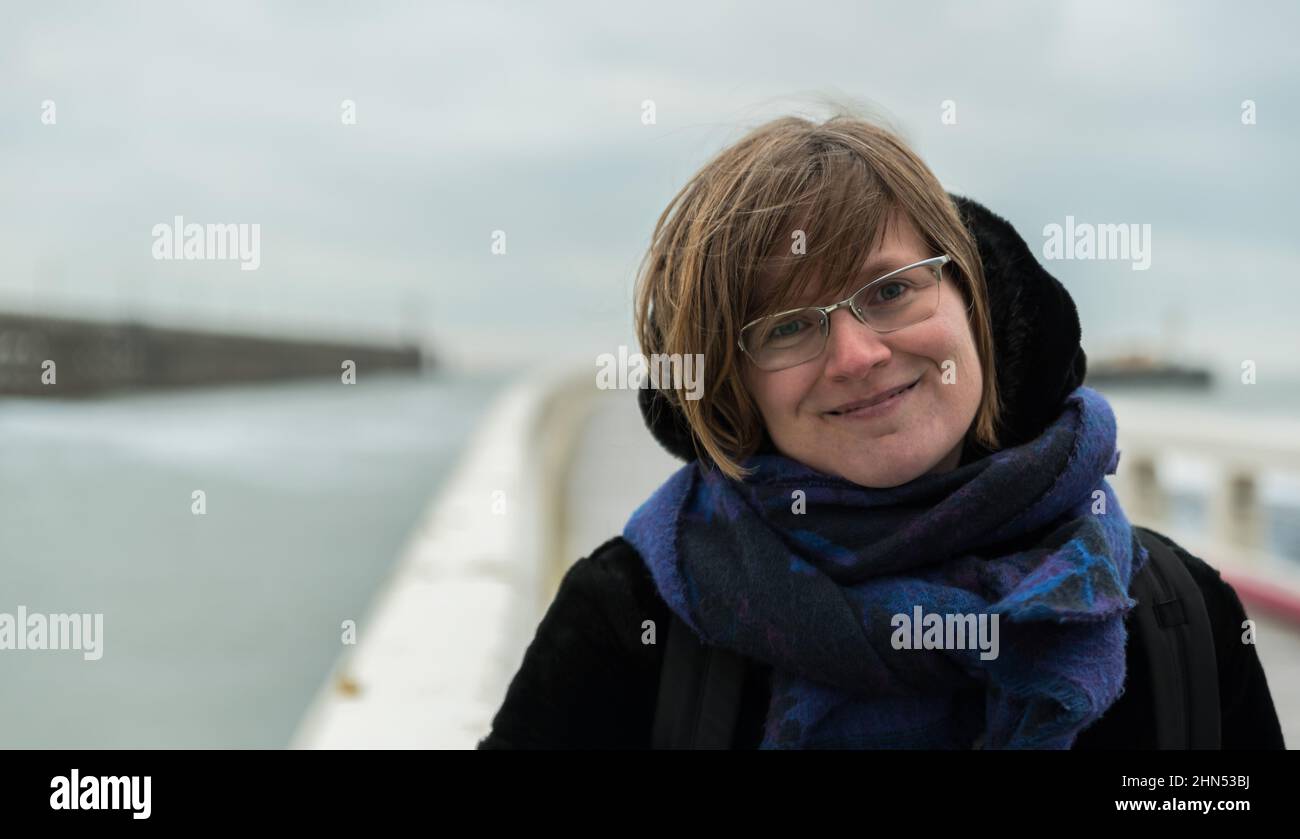 Porträt einer attraktiven weißen Frau, 30 Jahre alt mit Winterkleidung an einem windigen Tag am Meer, Blankenberge, Belgien Stockfoto