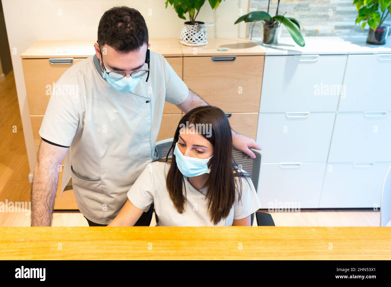 Weibliche und männliche Rezeptionisten verwenden eine Gesichtsmaske, während sie an der Rezeption eines Gesundheitszentrums arbeiten. Stockfoto