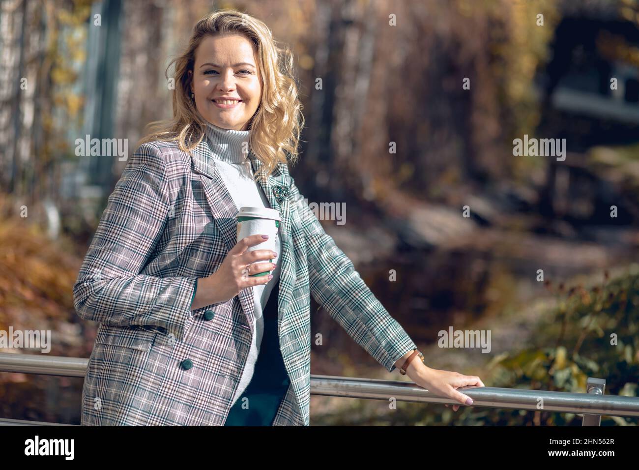 Porträt einer attraktiven lächelnden Frau mittleren Alters in karierter Jacke und grauem Rollkragen-Pullover stehen auf Metallbrücke. Stockfoto