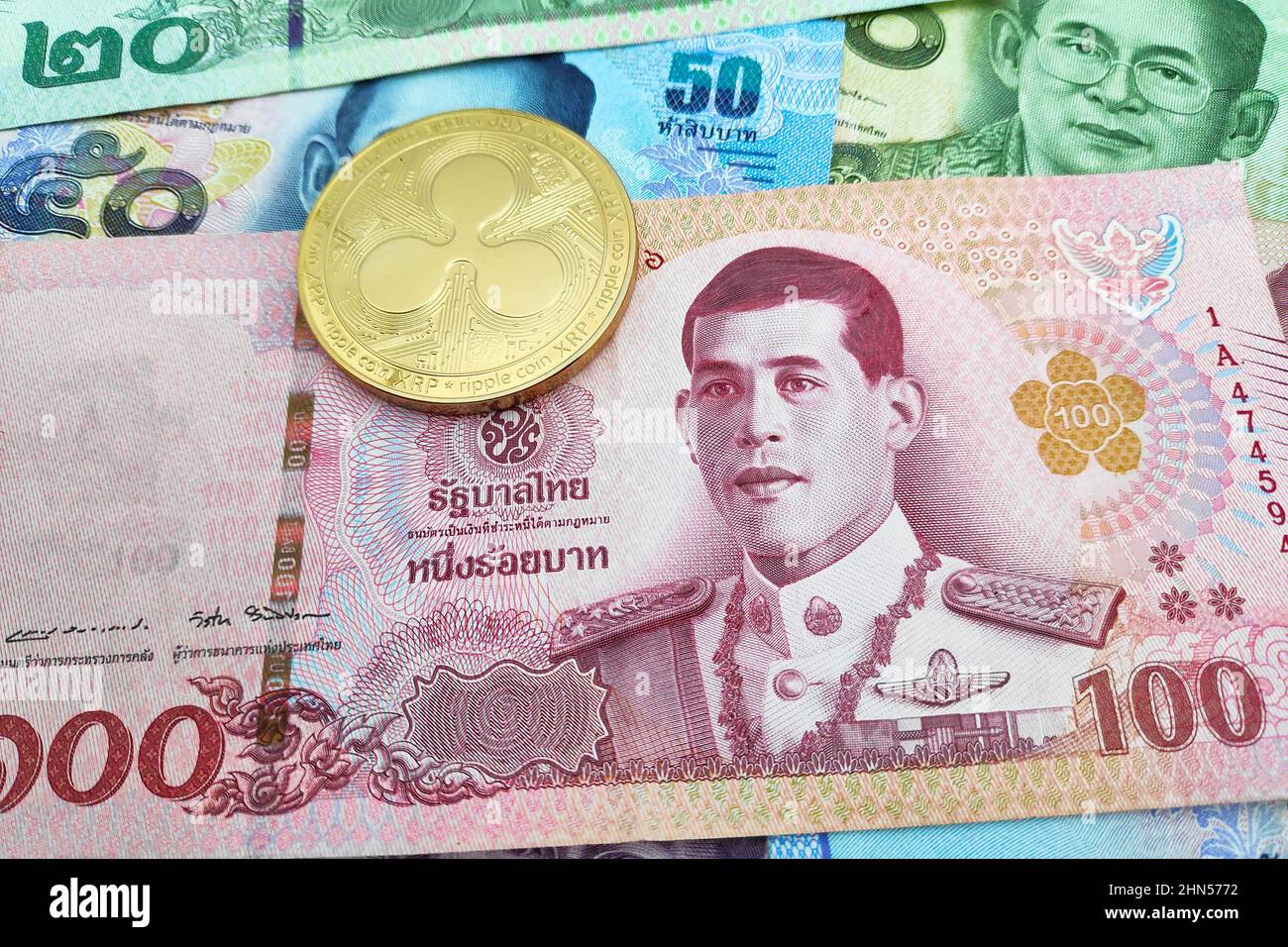 Nahaufnahme einer goldenen Ripple-Münze auf einem Stapel thailändischer Baht-Banknoten. Stockfoto