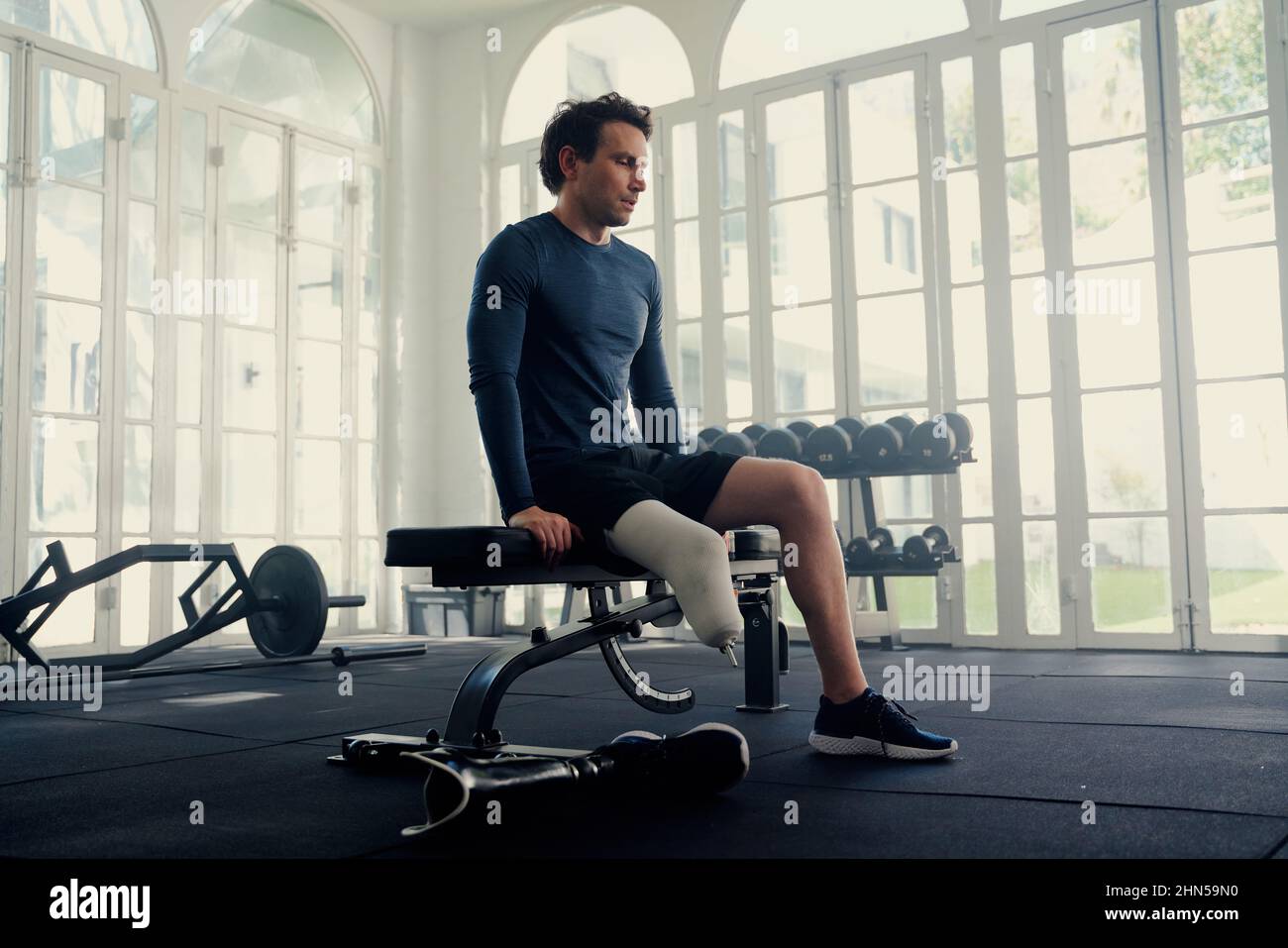 Mann mit Beinprothese sitzt auf einer Turnbank. Er bereitet sich mental auf seine Fitness vor Stockfoto