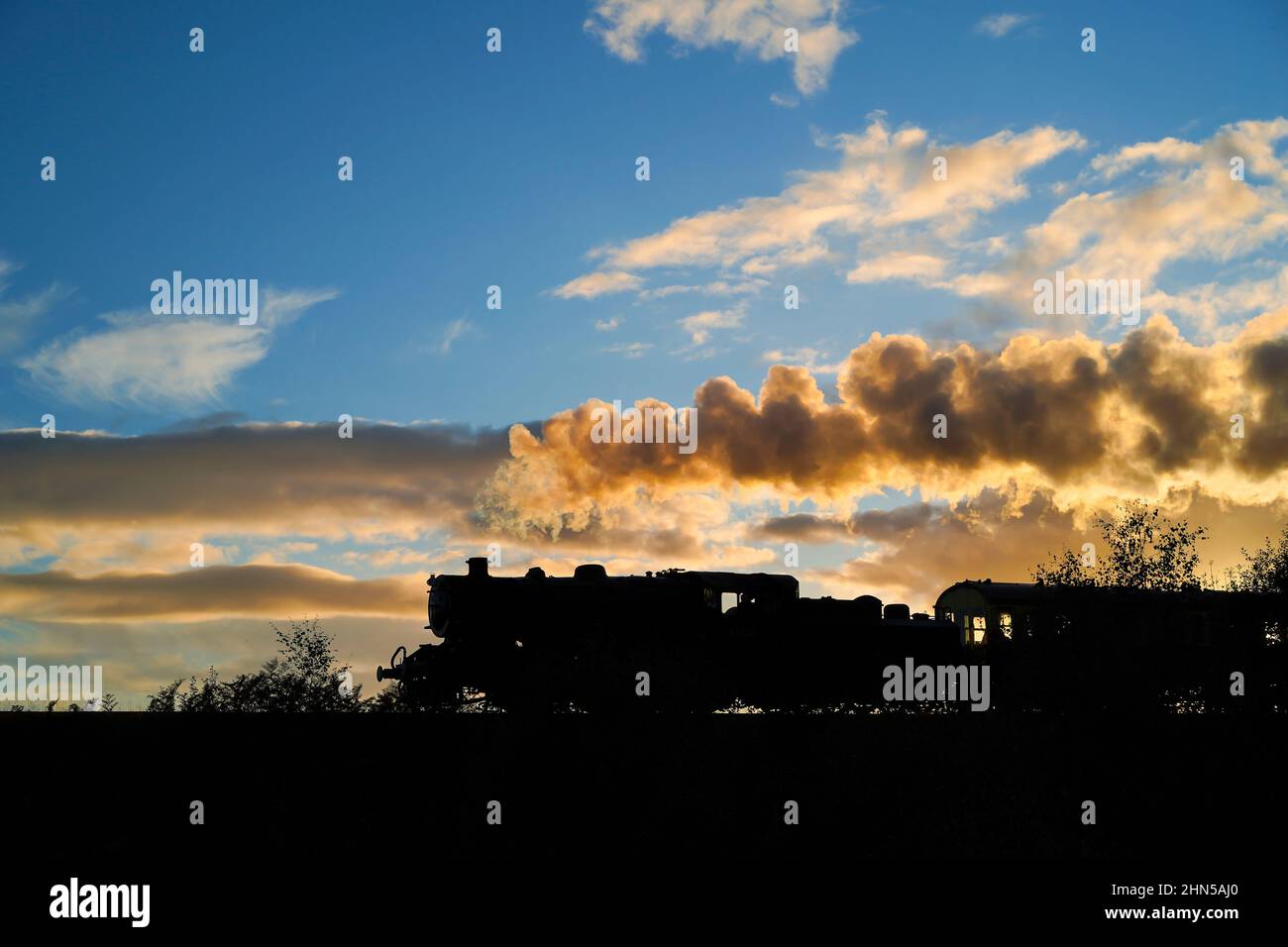 Silhouette einer alten britischen Dampfeisenbahn (Lokomotive und Kutsche), die in der Abenddämmerung entlang der Severn Valley Railway verläuft und einen dramatischen Sonnenuntergang bietet. Stockfoto