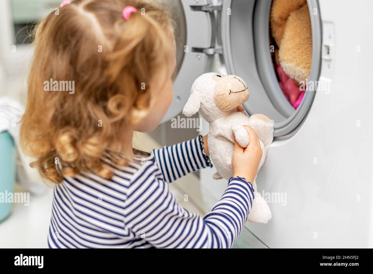 Das Kind beobachtet, wie die Waschmaschine waschen wird. Stockfoto