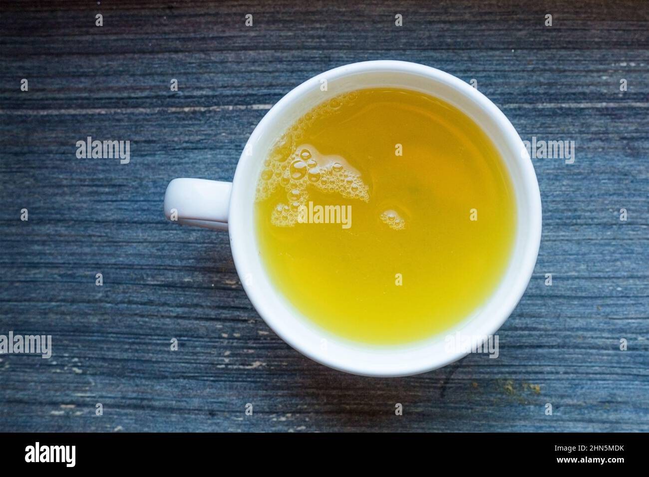 Weißer runder Porzellanbecher mit frischem Kräutertee aus grünem Tee. Warmes, gesundes Getränk zum Frühstück. Holzhintergrund. Draufsicht geometrische Komposition Stockfoto