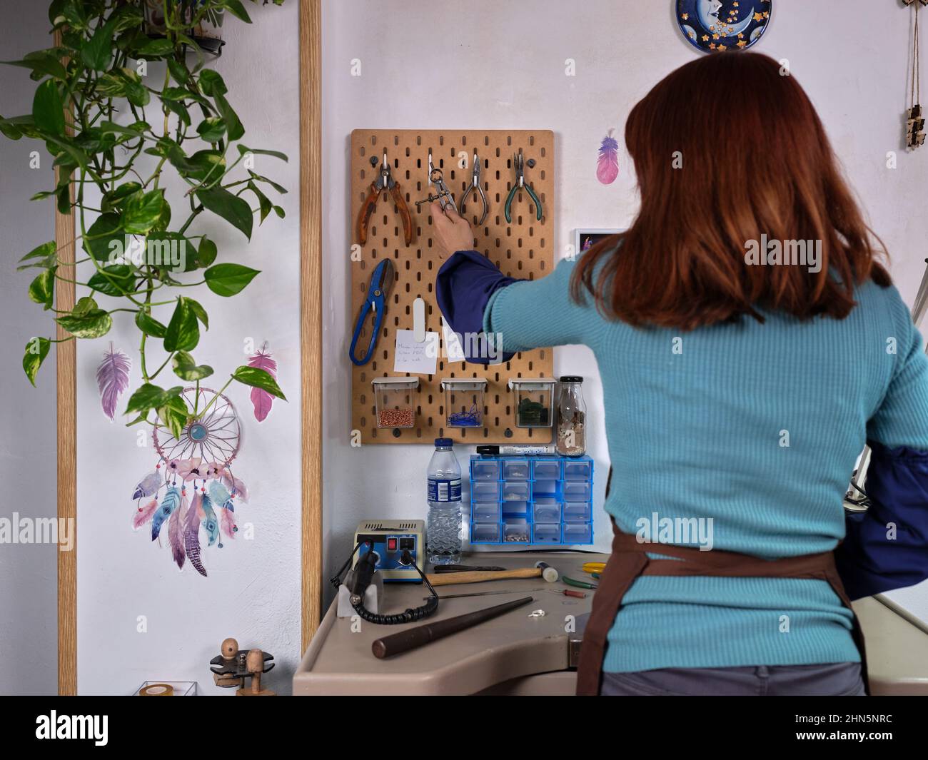 Eine Arbeiterin hängt ihre Werkzeuge auf, die sie gerade in ihrer Schmuckwerkstatt verwendet hat. Stockfoto
