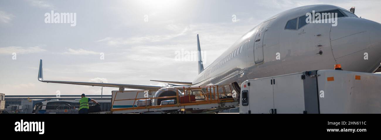 Arbeiter, die tagsüber Gepäck auf einem Förderband zu einem Flugzeug im Freien verladen Stockfoto