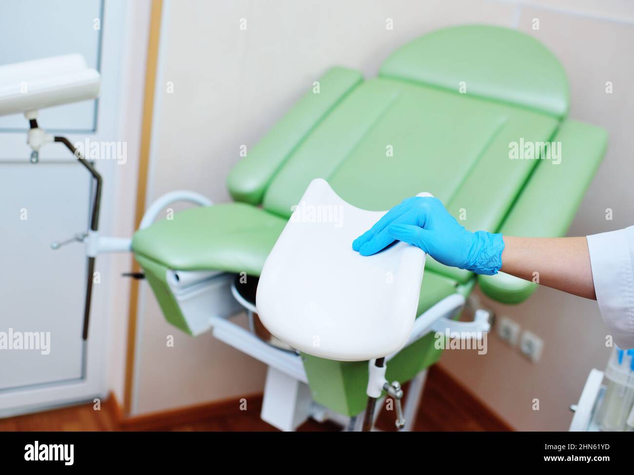 Der Gynäkologe, der Gummihandschuhe anzieht, bereitet sich auf die Untersuchung vor dem Hintergrund des gynäkologischen Stuhls vor. Stockfoto