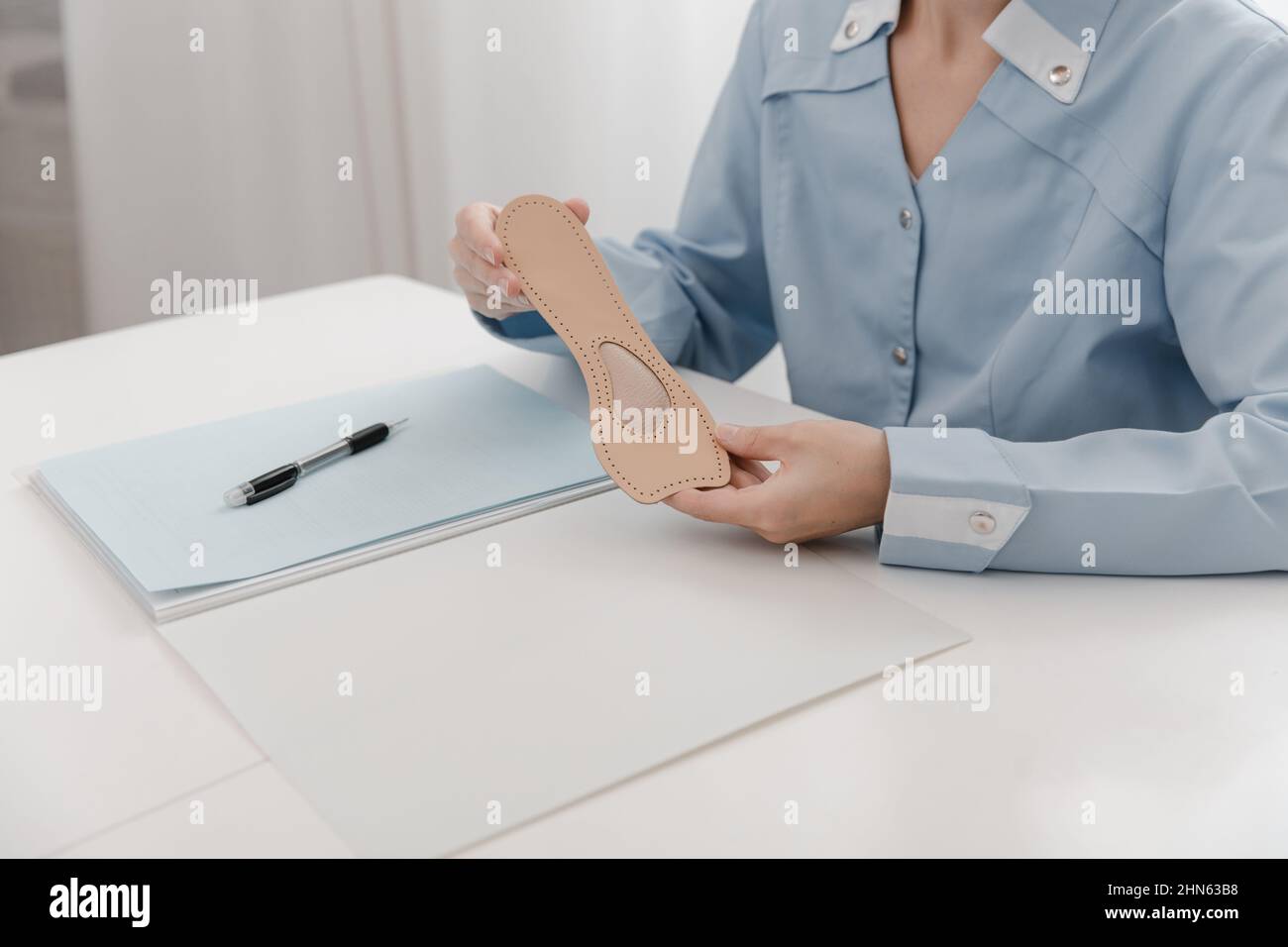 Arzt, der eine Einlegesohle hält, während er an einem Tisch sitzt. Orthopäde testet das medizinische Gerät. Orthopädische Einlagen. Fußpflege. Korrektur Der Flachen Füße Stockfoto