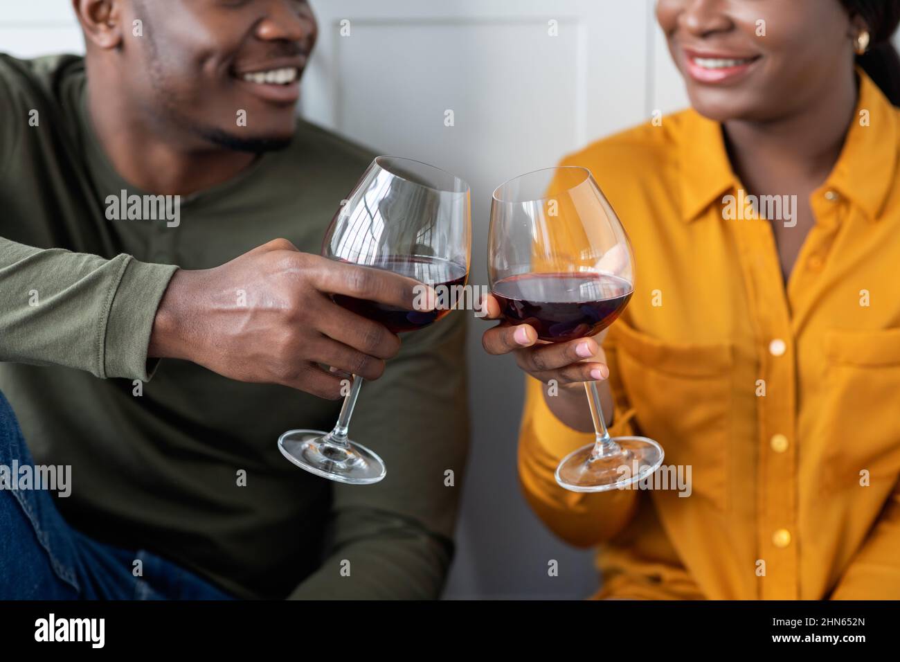 Toast Für Uns. Nahaufnahme Von Anklirrenden Gläsern Des Schwarzen Paares Mit Rotwein Stockfoto