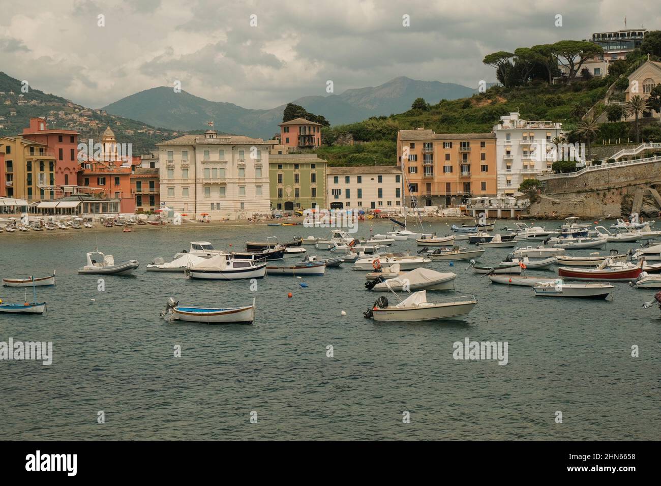 Boote und Yachten, die in der Bucht von Silence, Baia di Silenzio in Sestre-Levante, Ligurien, Italien, über die bunten Gebäude, Berge und Himmel schweben. Stockfoto