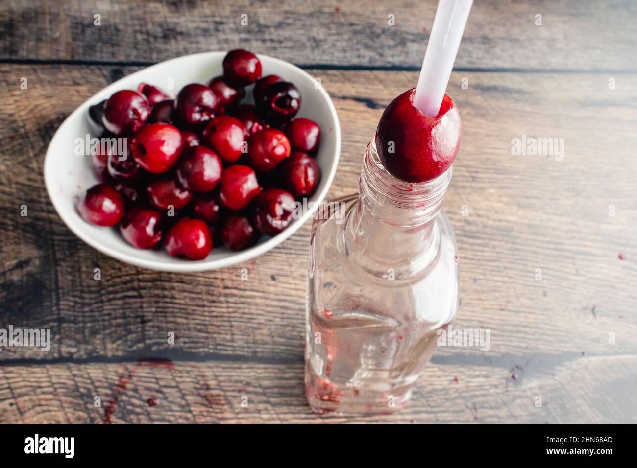 Verwenden eines Trinkhalms und einer Flasche, um frische Kirschen zu pitchen: Frische Kirschen mit einem Plastikstroh und einer Glasflasche pitchen Stockfoto