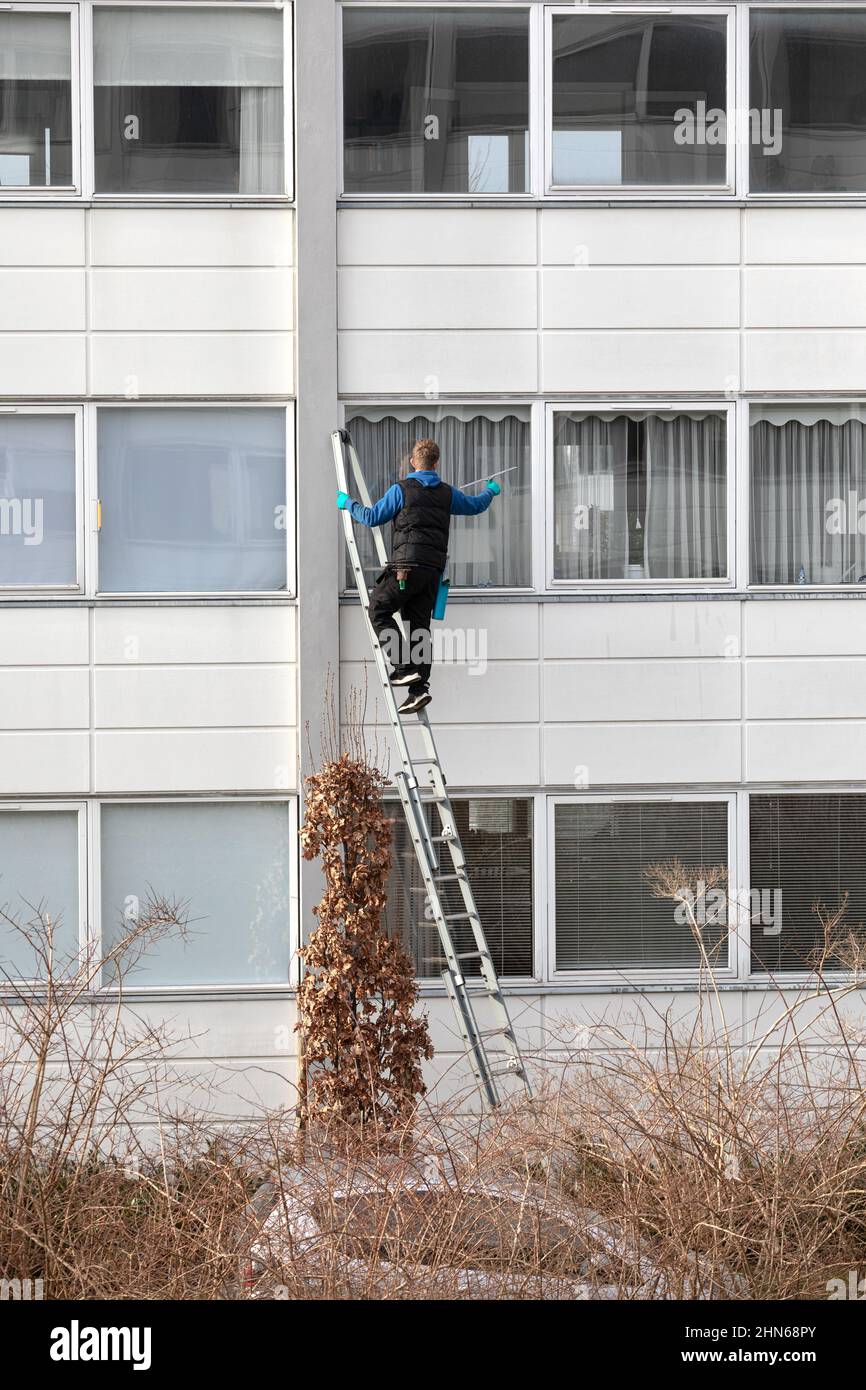 Arbeiter auf einer Leiter, der die Außenfenster des Wohngebäudes reinigte Stockfoto