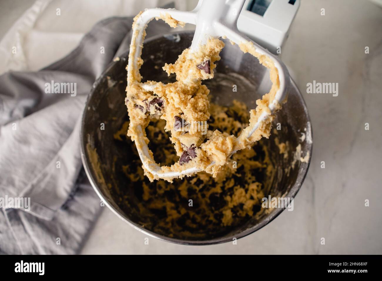 Standmixer Paddle-Aufsatz mit Plätzchenteig bedeckt: Nahaufnahme eines Standmixer-Quirl, der mit Schokoladenchip-Plätzchenteig bedeckt ist Stockfoto