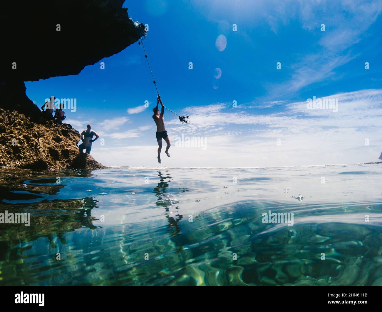 Im Sommer schaukelt der Teenager am Seil über blaues Wasser Stockfoto