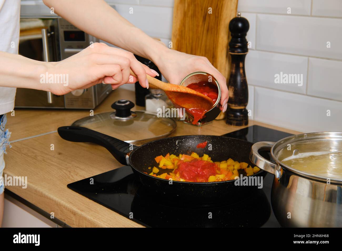 Nahaufnahme der weiblichen Hand, die während der Zubereitung von Pasta-Sauce ganze geschälte Tomaten in die Bratpfanne gegeben hat Stockfoto