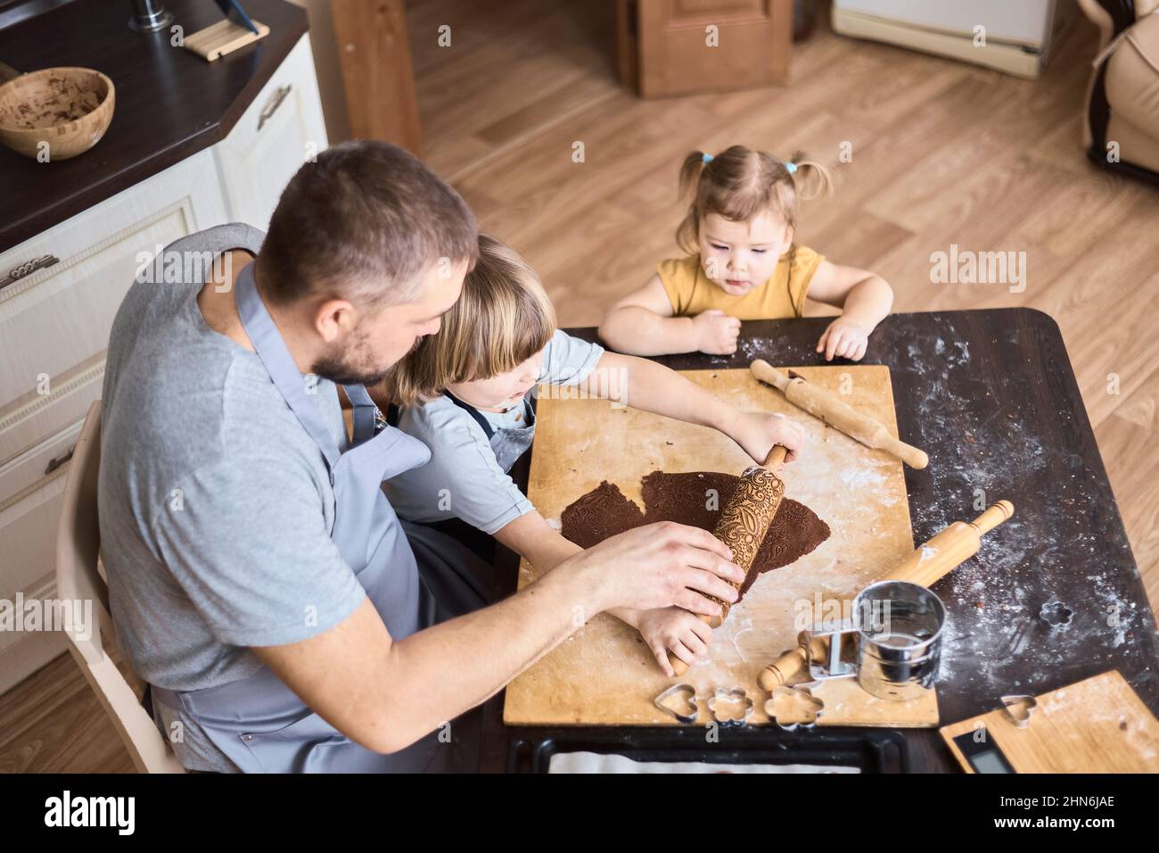 Vater und zwei Kinder rollten den Schokoladenkeketeig aus Stockfoto