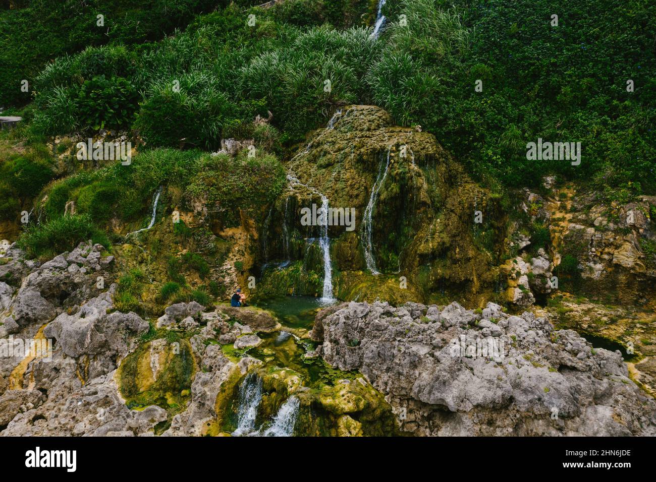 Die Person sitzt am Gezeitenpool, der von Klippen-Wasserfällen geschaffen wird Stockfoto