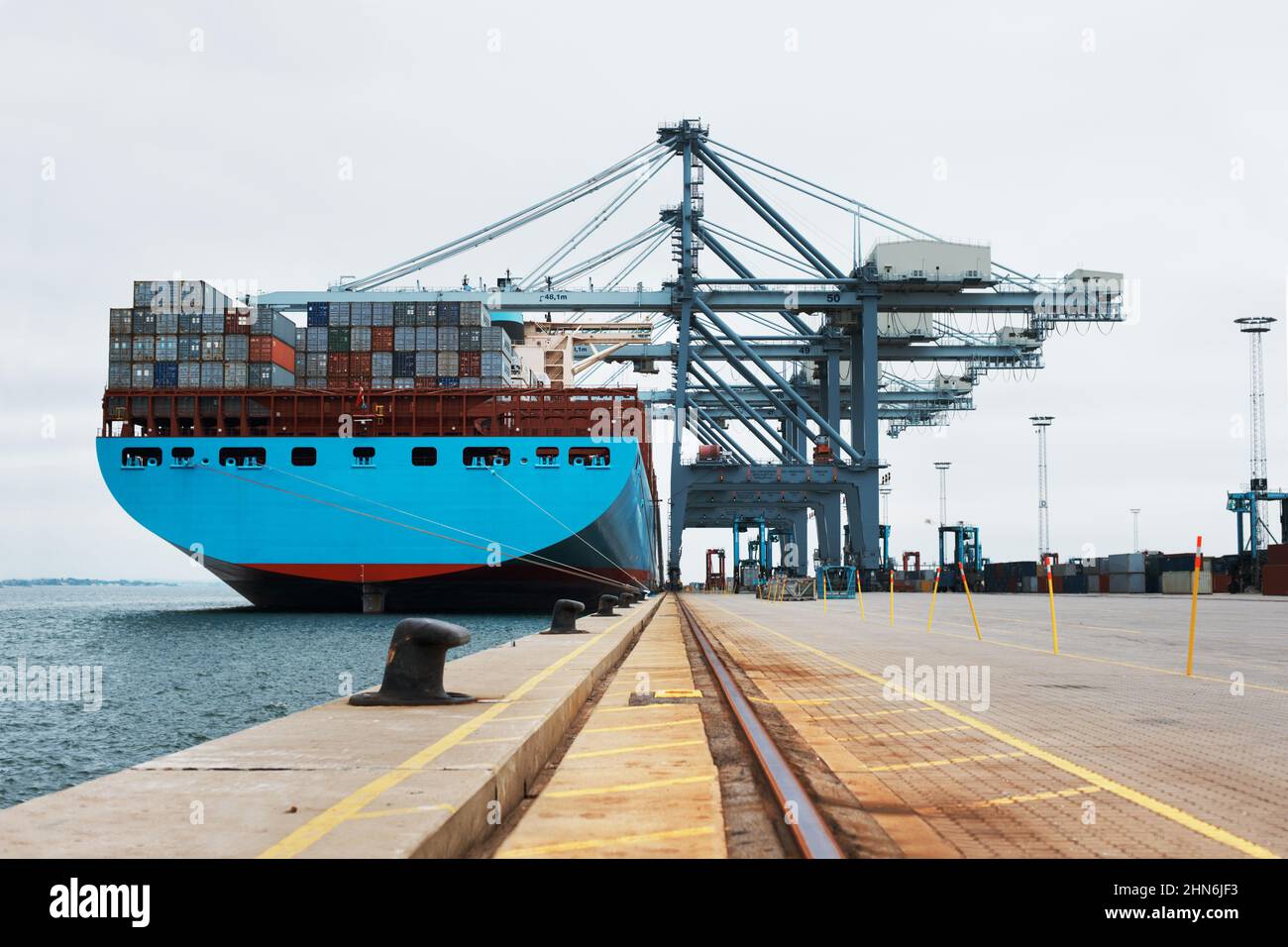 Ladungsverladung. Ein massives Frachtschiff, das am Hafen festgemacht wurde, wurde mit Containern beladen. Stockfoto