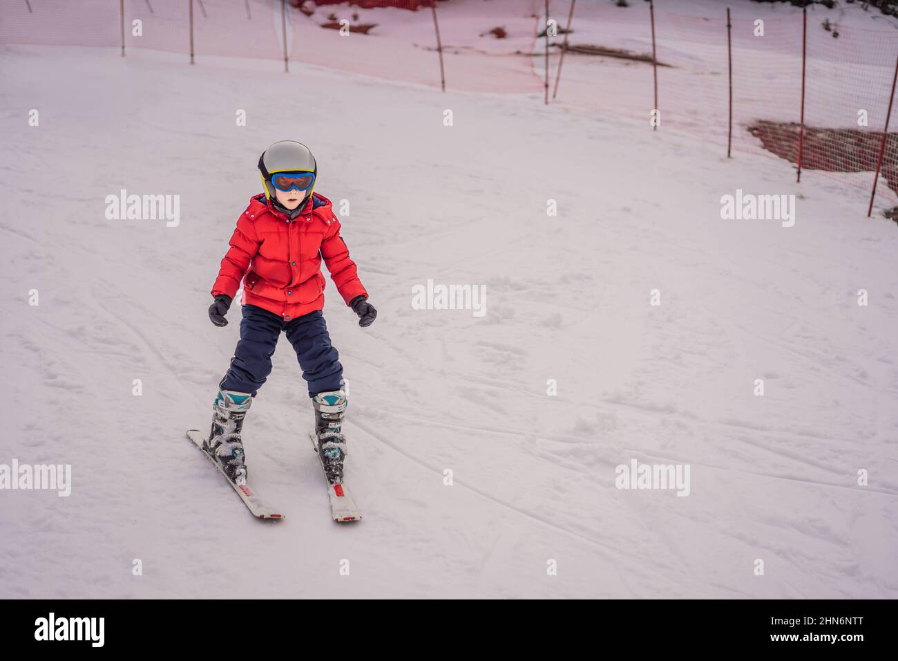 Kinder Skifahren in den Bergen. Aktives Kleinkind mit Schutzhelm, Schutzbrille und Stöcken. Skirennen für kleine Kinder. Wintersport für die ganze Familie. Kinder Ski Stockfoto