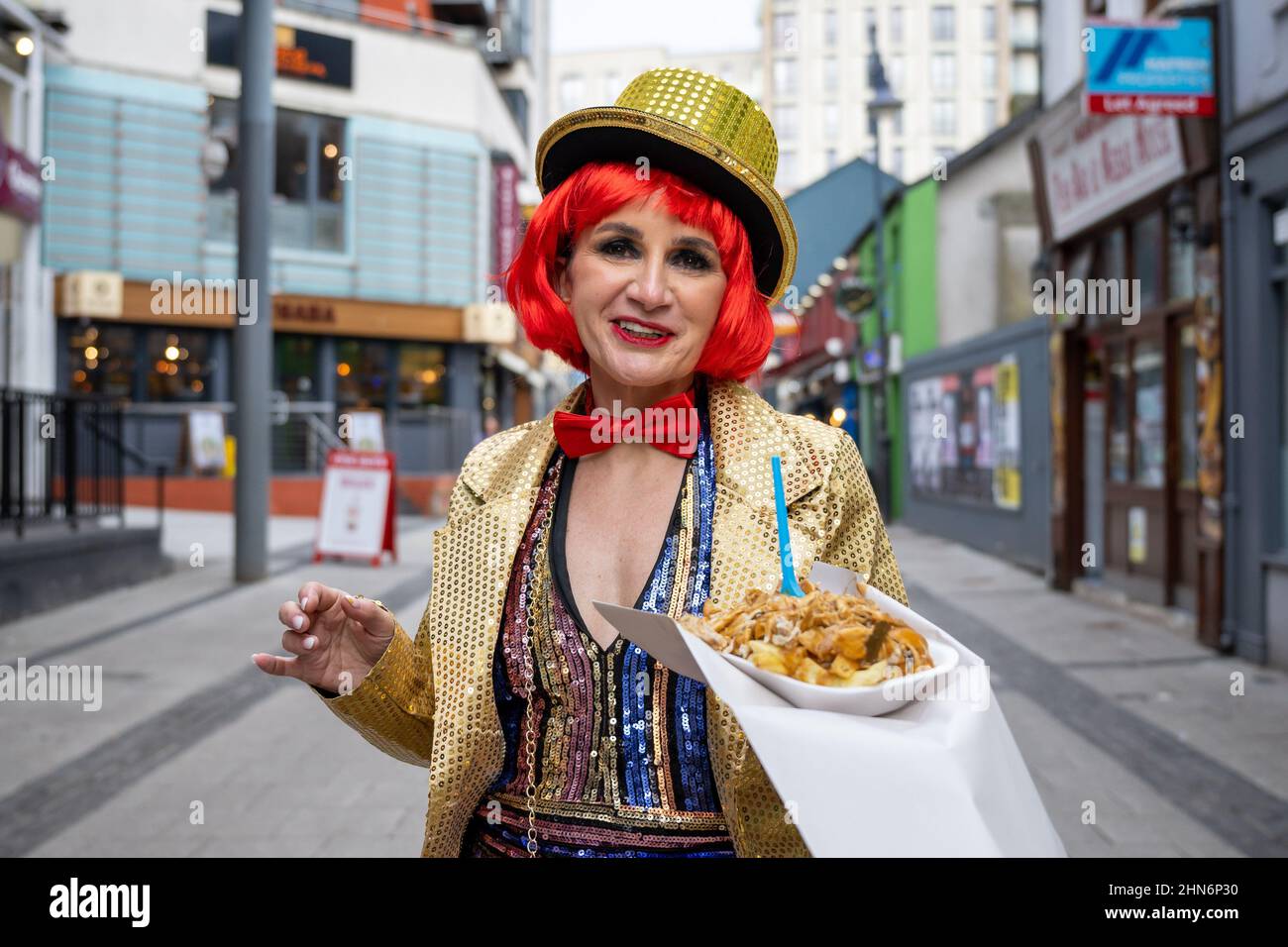 Eine Frau, die als Figur aus der Rocky Horror Show gekleidet ist, posiert für ein Foto, das Essen zum Mitnehmen in der Caroline Street in Cardiff, Wales, Großbritannien, hält. Stockfoto