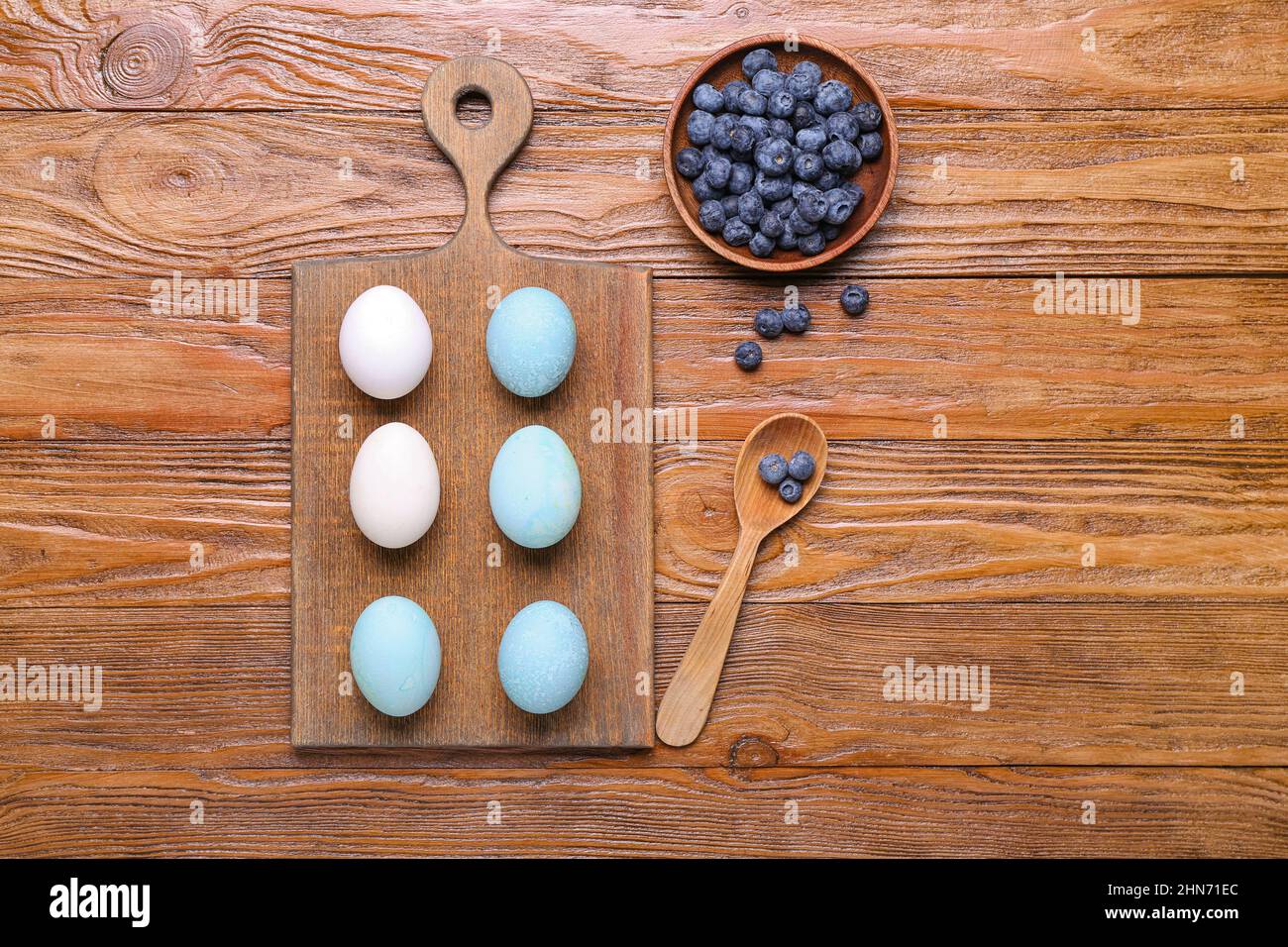 Brett mit selbstgemachten gefärbten Ostereiern und Schale mit Heidelbeere auf Holzhintergrund Stockfoto