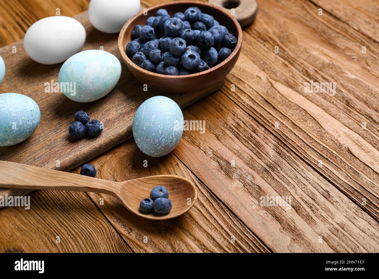 Hausgemachte gefärbte Ostereier und Schüssel mit Heidelbeere auf Holztisch, Nahaufnahme Stockfoto