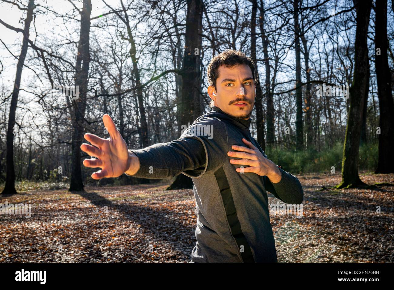 Läufer macht Stretching im Wald. Junger Mann mit blauen Augen und Schnurrbart trainiert im Park. Stockfoto
