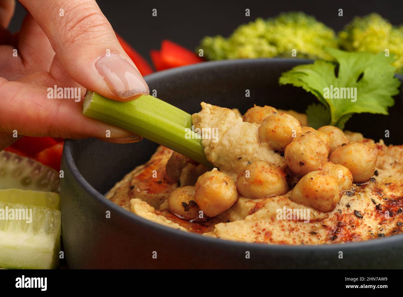 Nahaufnahme der Hand mit Sellerie-Stick mit Kichererbsen-Hummus. Leckerer Hummus mit Gemüse und geräuchertem Paprika Stockfoto